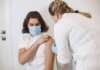 A healthcare worker wearing a mask gives a vaccine shot to a patient in a medical office.