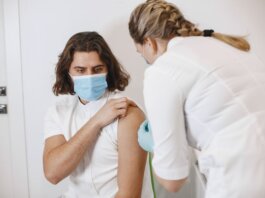 A healthcare worker wearing a mask gives a vaccine shot to a patient in a medical office.