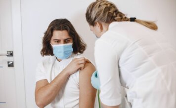 A healthcare worker wearing a mask gives a vaccine shot to a patient in a medical office.
