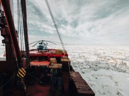 A helicopter on the deck of an icebreaker ship navigating through icy Arctic waters.