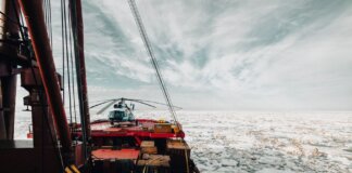 A helicopter on the deck of an icebreaker ship navigating through icy Arctic waters.