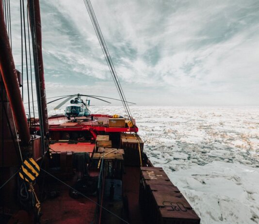 A helicopter on the deck of an icebreaker ship navigating through icy Arctic waters.