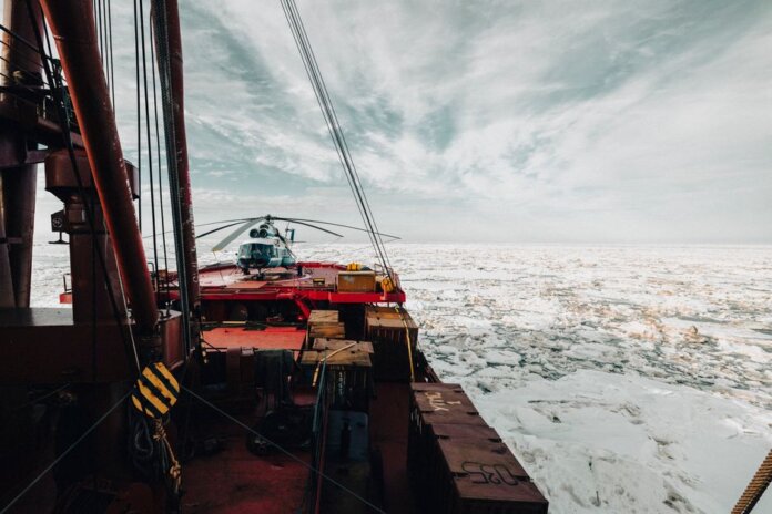 A helicopter on the deck of an icebreaker ship navigating through icy Arctic waters.