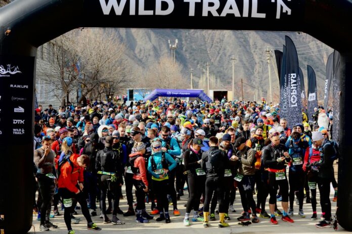 A large group of runners prepares for an exciting outdoor marathon race under a Wild Trail arch. A large group of runners prepares for an exciting outdoor marathon race under a Wild Trail arch.