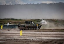 A military tank firing a shell during training in an open field.