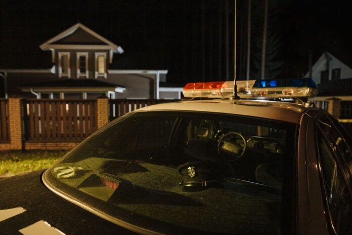 A parked police car at night in front of suburban houses with lights on, creating a dramatic mood.
