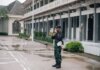 A security guard stands alert with a megaphone outside a building after rain.