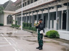A security guard stands alert with a megaphone outside a building after rain.