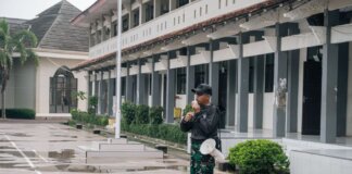 A security guard stands alert with a megaphone outside a building after rain.
