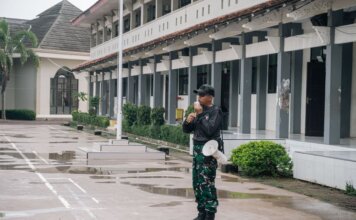 A security guard stands alert with a megaphone outside a building after rain.