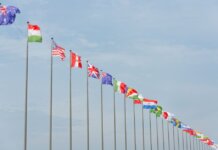 A series of international flags flying in a line against a clear blue sky, symbolizing global unity.
