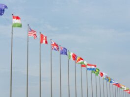 A series of international flags flying in a line against a clear blue sky, symbolizing global unity.