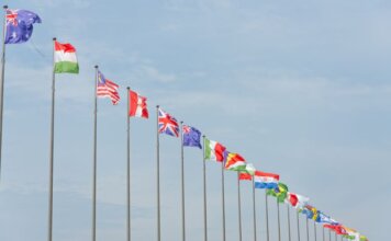 A series of international flags flying in a line against a clear blue sky, symbolizing global unity.