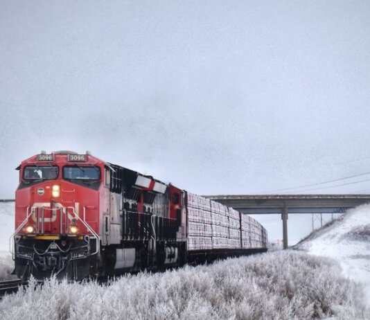 A striking red freight train travels through snowy Grasswood, Saskatchewan, on a winter day.