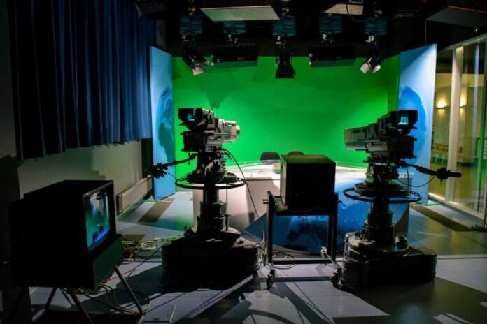 A TV studio setup featuring cameras and a green screen for production purposes. A TV studio setup featuring cameras and a green screen for production purposes.