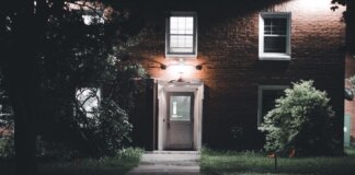 A warmly lit brick house entrance under a night sky, featuring a serene garden setting.