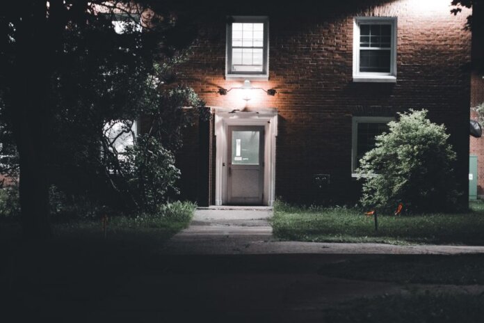 A warmly lit brick house entrance under a night sky, featuring a serene garden setting. A warmly lit brick house entrance under a night sky, featuring a serene garden setting.