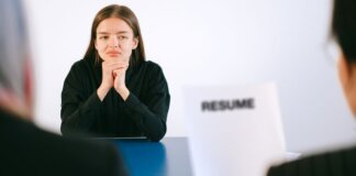 A woman in a job interview facing two employers with a focus on her resume.