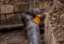 A worker welds a pipe in an urban trench, showcasing industrial construction work.