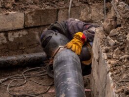 A worker welds a pipe in an urban trench, showcasing industrial construction work.