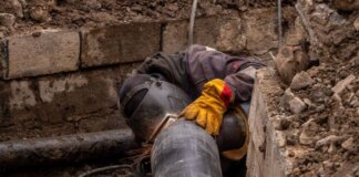 A worker welds a pipe in an urban trench, showcasing industrial construction work.