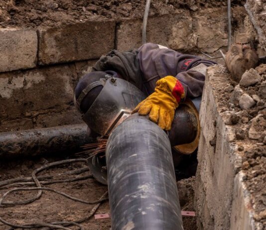 A worker welds a pipe in an urban trench, showcasing industrial construction work.
