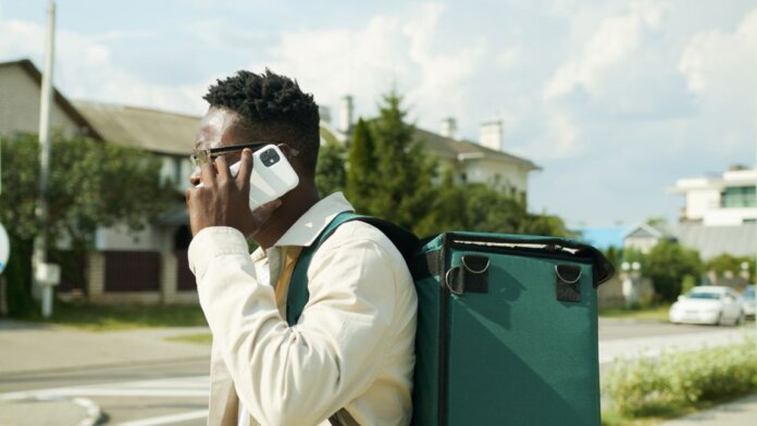 A young delivery man talks on his smartphone while carrying a thermal delivery bag outdoors.