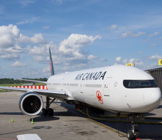 Air Canada Boeing 777 airplane parked at an airport gate under a clear blue sky.