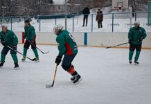 Amateur ice hockey match in snow-filled setting with players in green uniforms.