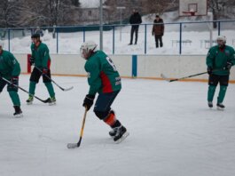 Amateur ice hockey match in snow-filled setting with players in green uniforms.