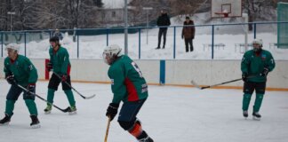 Amateur ice hockey match in snow-filled setting with players in green uniforms.