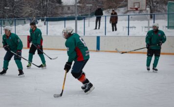 Amateur ice hockey match in snow-filled setting with players in green uniforms.