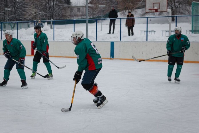 Amateur ice hockey match in snow-filled setting with players in green uniforms. Amateur ice hockey match in snow-filled setting with players in green uniforms.