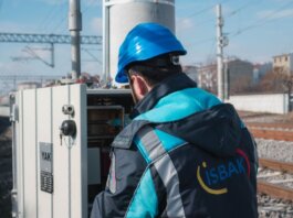 An engineer in a blue hard hat examines a fuse box on a railway track outdoors.
