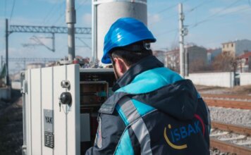 Электронный техник SkyTrain — о ночных сменах и карьере в рабочих профессиях An engineer in a blue hard hat examines a fuse box on a railway track outdoors.
