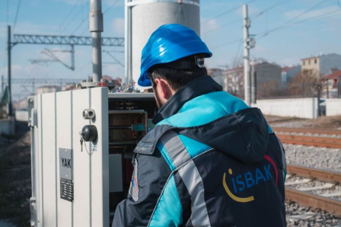 An engineer in a blue hard hat examines a fuse box on a railway track outdoors. An engineer in a blue hard hat examines a fuse box on a railway track outdoors.