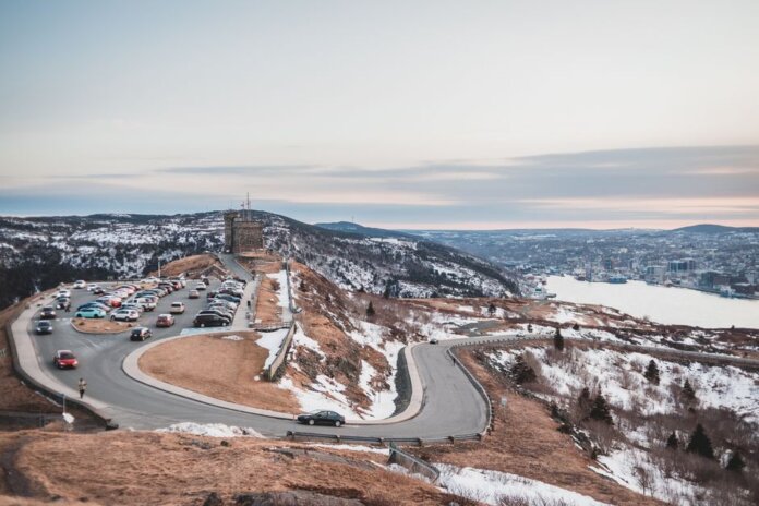 Automobiles riding on curvy asphalt roadway near grassy shore covered with snow against river and cloudy sky on winter day Automobiles riding on curvy asphalt roadway near grassy shore covered with snow against river and cloudy sky on winter day