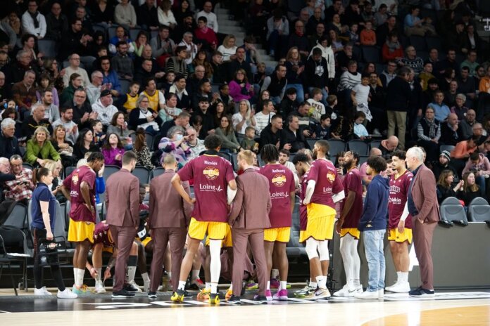 Basketball team huddles on court during a game timeout with audience in background. Basketball team huddles on court during a game timeout with audience in background.