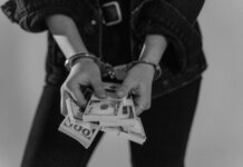 Black and white image of a handcuffed person holding bundles of US dollars.
