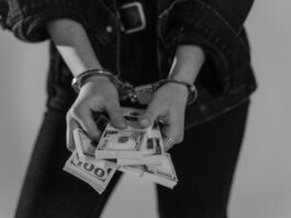 Black and white image of a handcuffed person holding bundles of US dollars.