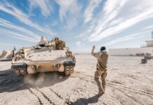 Bradley Fighting Vehicle and soldier in desert training operation under clear sky.