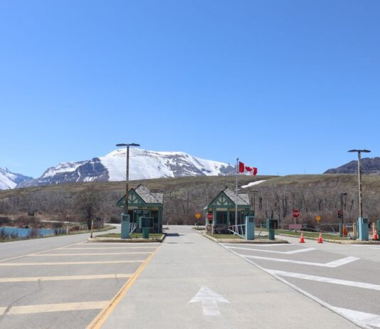 Canadian border crossing amidst stunning snow-capped mountains and clear blue sky.