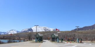 Canadian border crossing amidst stunning snow-capped mountains and clear blue sky.