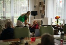 Caregiver assisting elderly women with tea in a cozy nursing home setting.