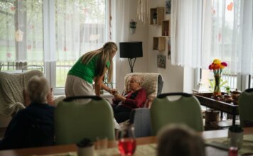 Caregiver assisting elderly women with tea in a cozy nursing home setting.