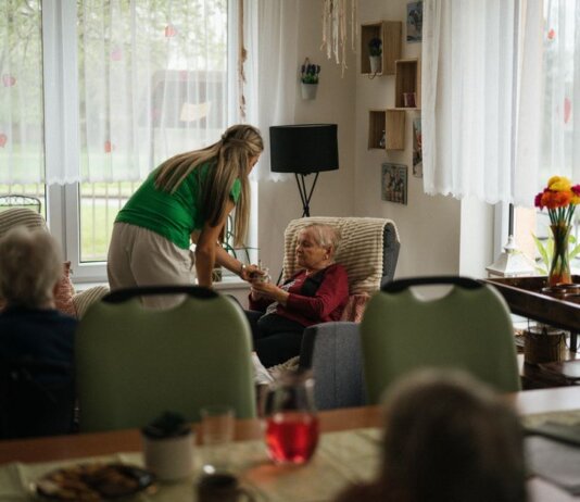 Caregiver assisting elderly women with tea in a cozy nursing home setting.