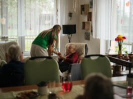 Caregiver assisting elderly women with tea in a cozy nursing home setting.