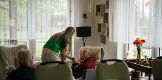 Caregiver assisting elderly women with tea in a cozy nursing home setting.