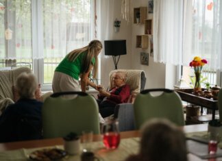 Caregiver assisting elderly women with tea in a cozy nursing home setting.