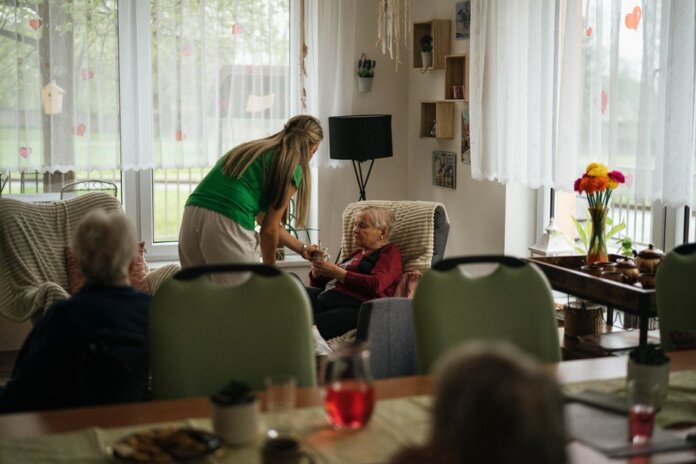 Caregiver assisting elderly women with tea in a cozy nursing home setting. Caregiver assisting elderly women with tea in a cozy nursing home setting.